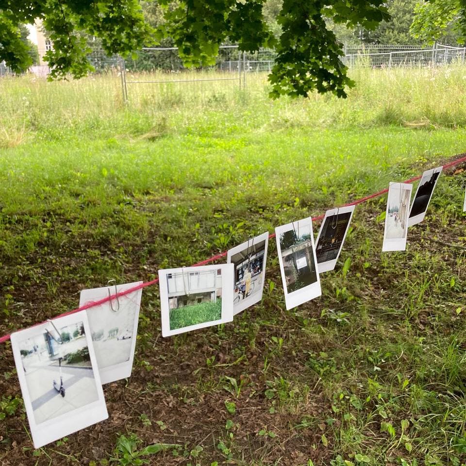 Wiese mit einer Wäscheleine, an der Papiere mit Fotografien hängen